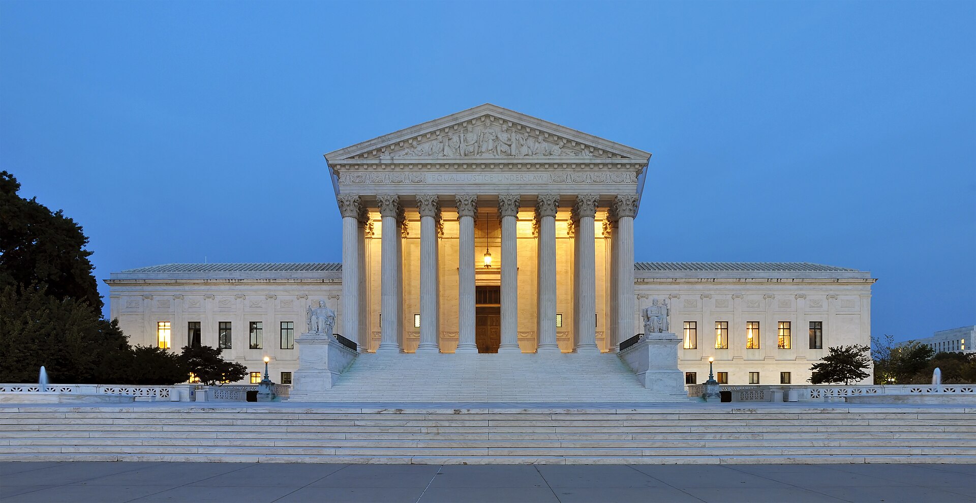 The west front of the United States Supreme Court Building at dusk, its marble columns and pediment lit against the evening sky.