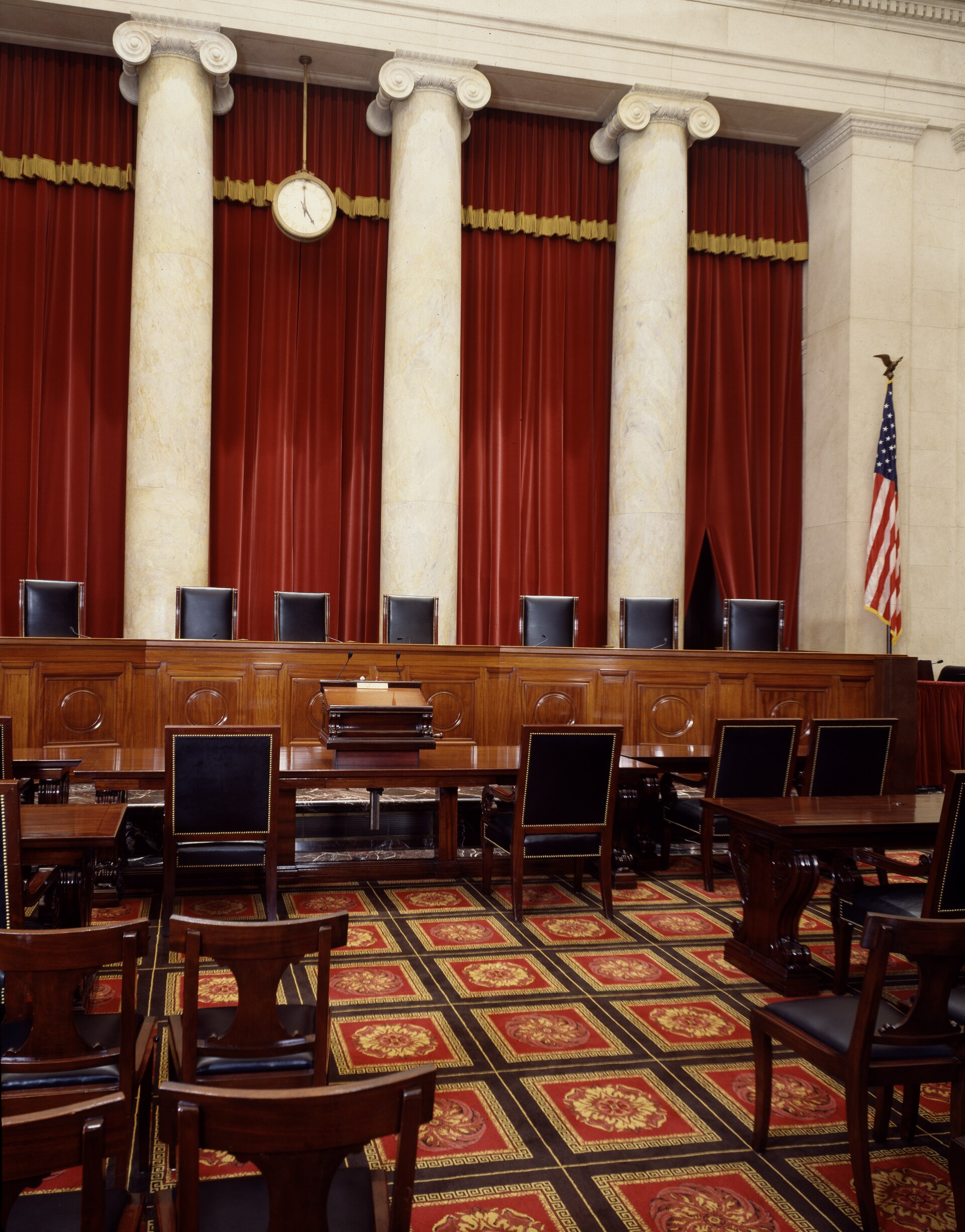 The justices' bench in the courtroom of the Supreme Court of the United States, its nine chairs empty beneath the marble columns.